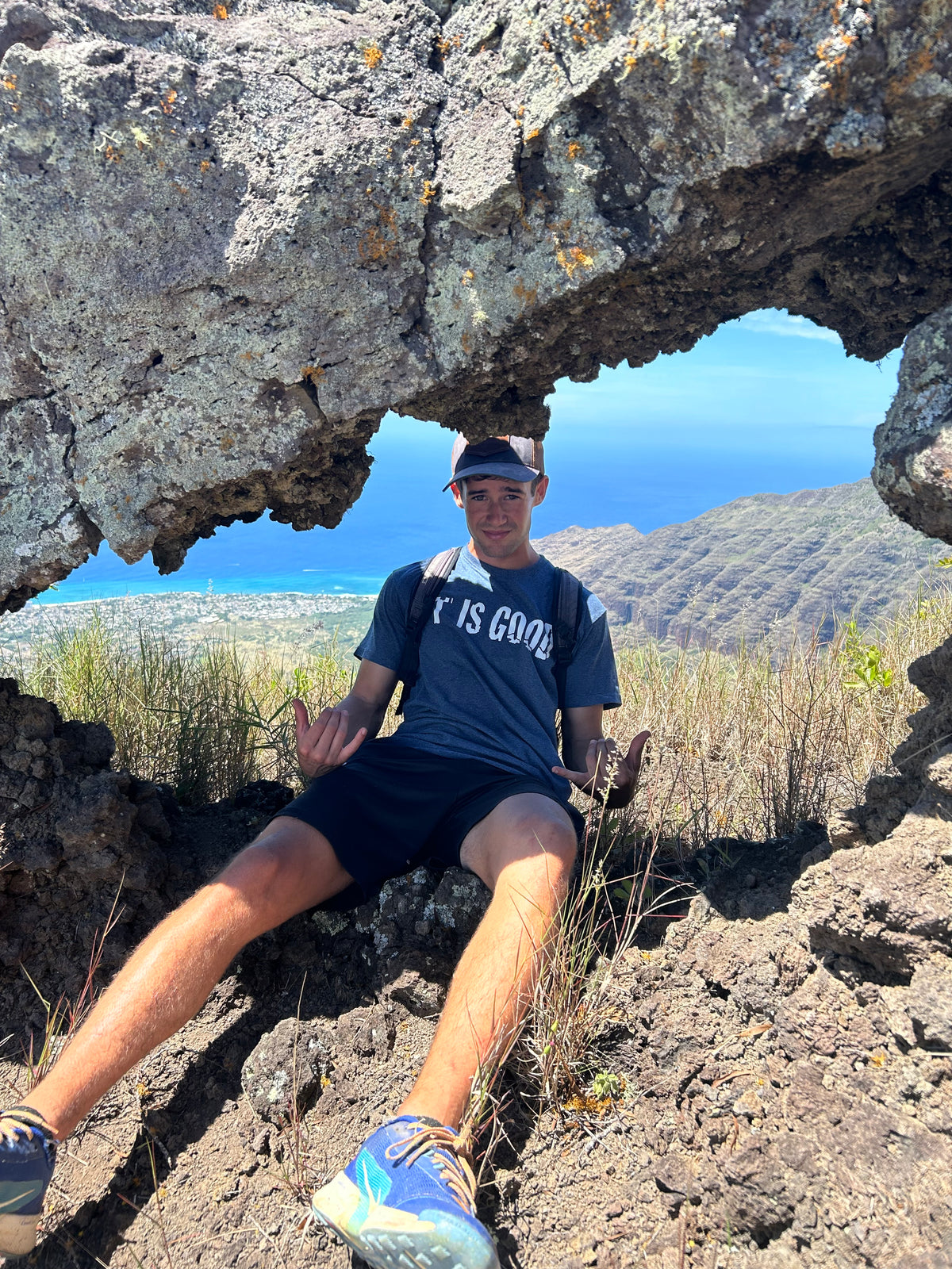 FIT IS GOOD Tee in Heather Blue, resting under a rock arch in Oahu, Hawaii